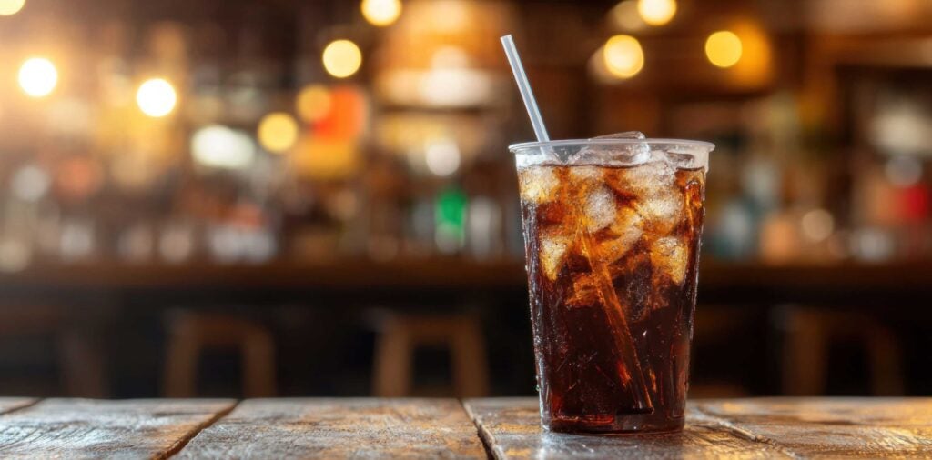 Glass of diet cola with a straw and ice sitting on a bar.
