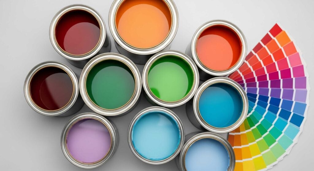 Overhead view of lid-less cans of paint in different colors. Next to the cans is a rainbow of color swatches.