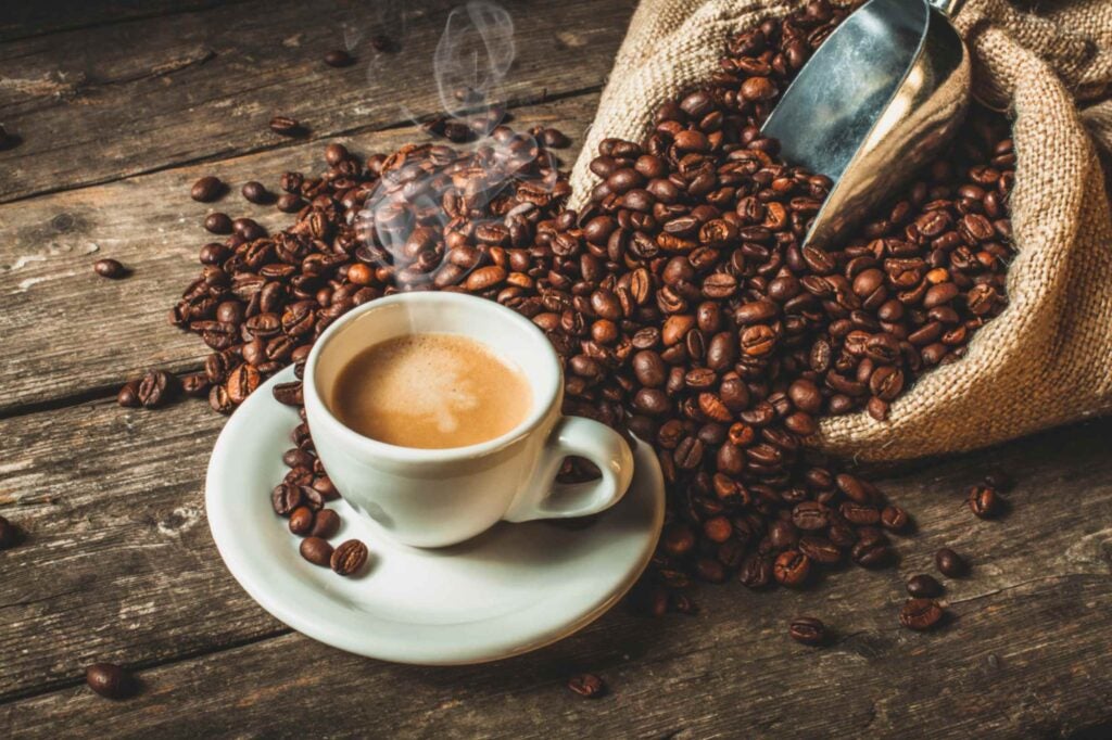 Cup of coffee next to a bag of coffee beans that are spilling out