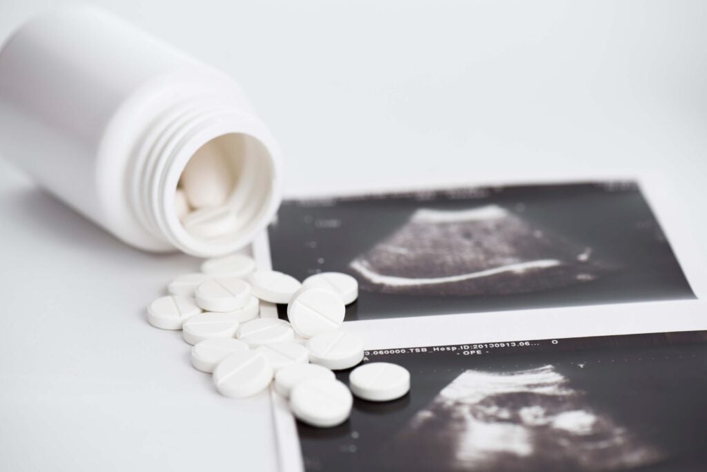 Pills spilling out of a bottle near ultrasound photos.