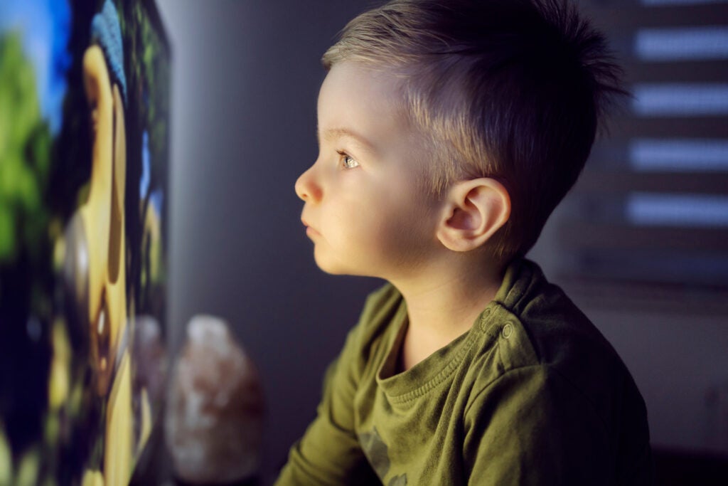 Young child sitting right in front of a television, staring into the screen.