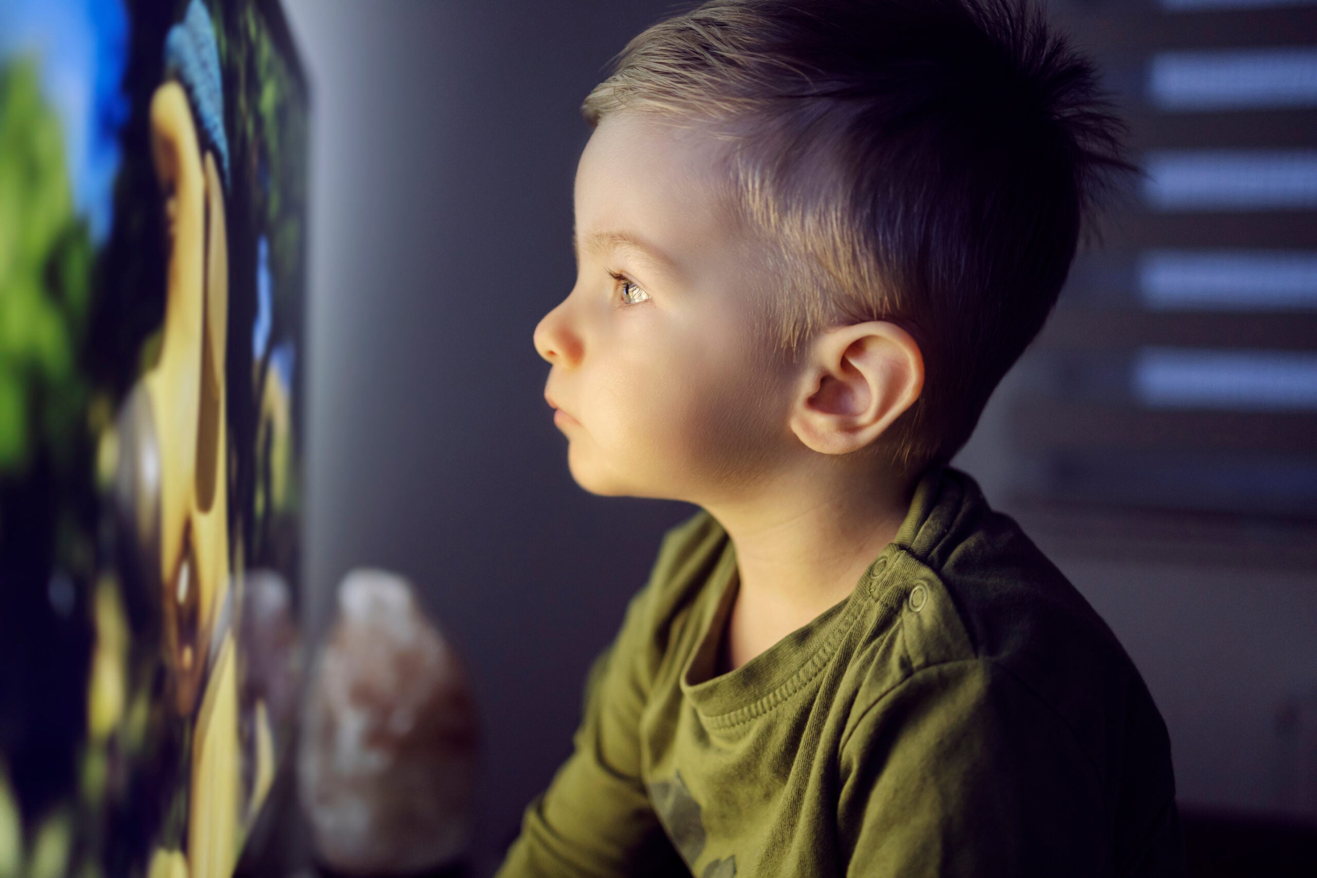 Young child sitting right in front of a television, staring into the screen.