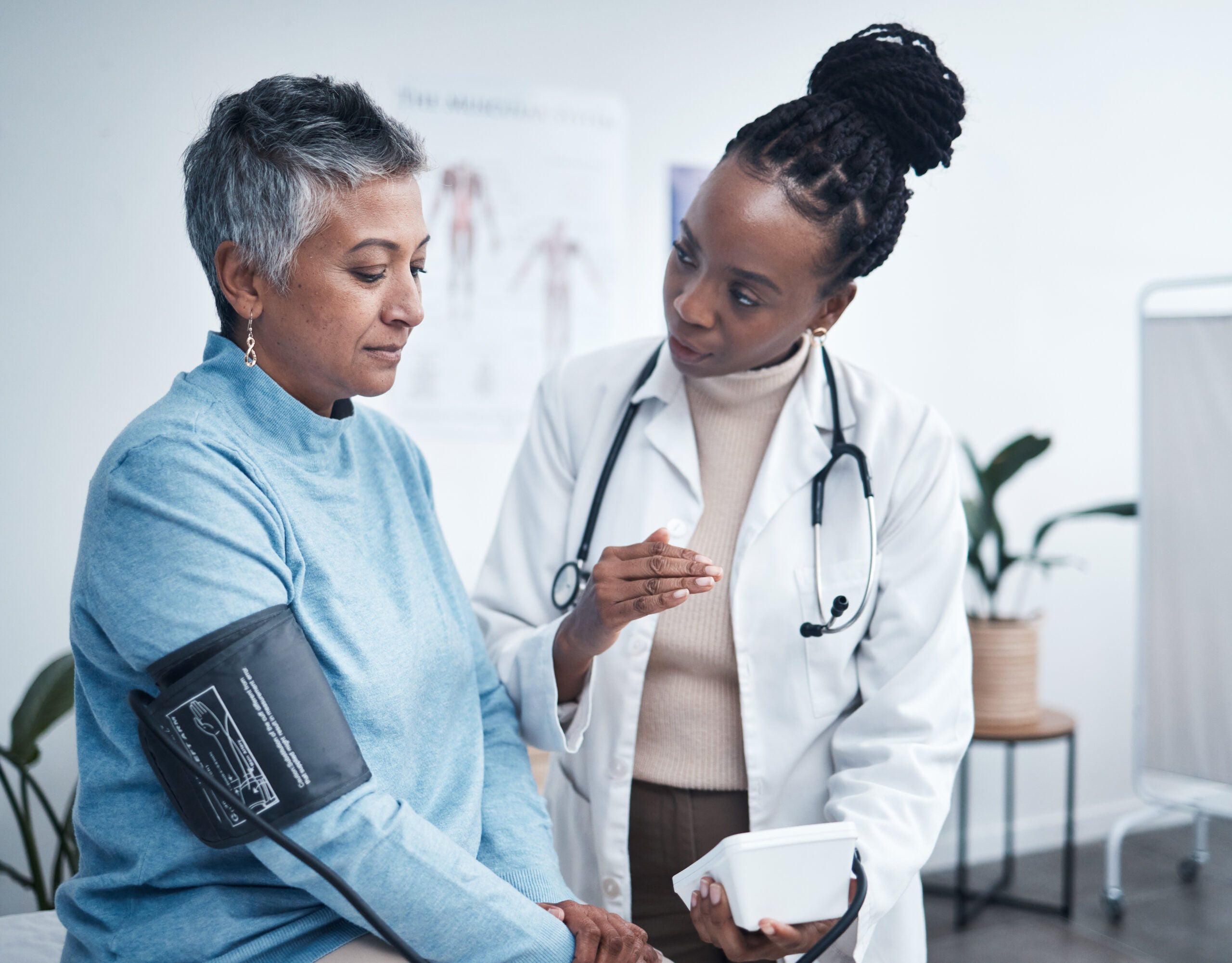 A female doctor in conversation with a patient who has a blood-pressure cuff on and appears to be in the middle of an exam.