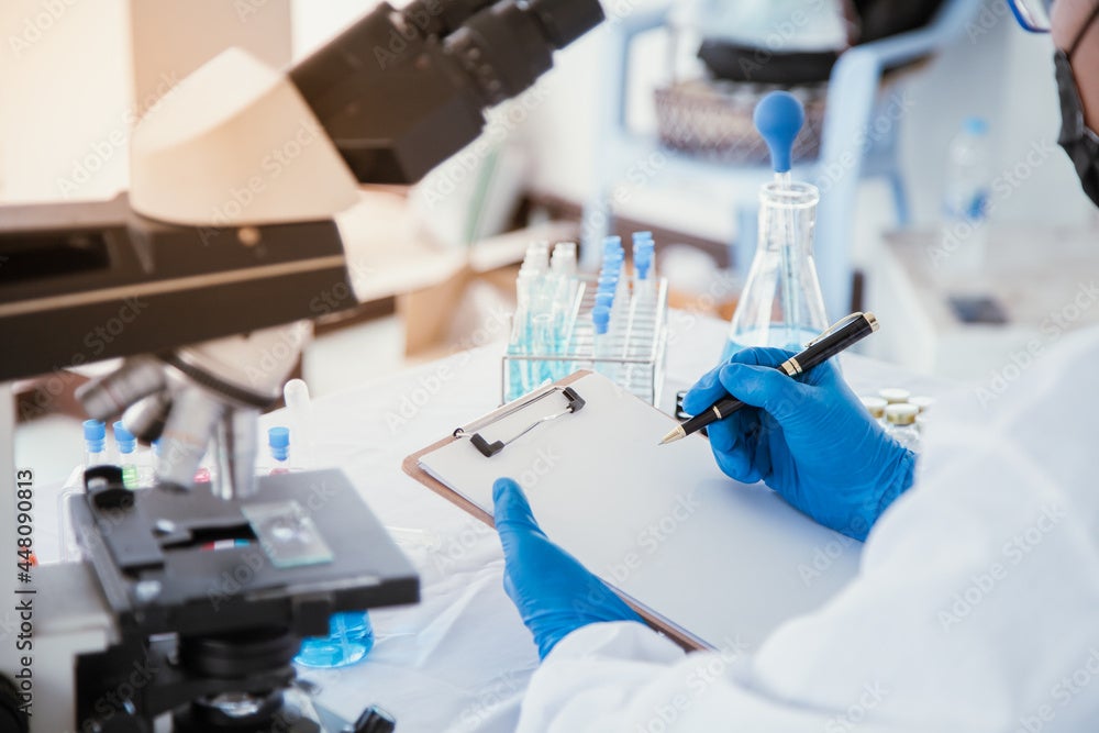 Person working in a lab...just their gloved hands and forearms in a white coat are visible.