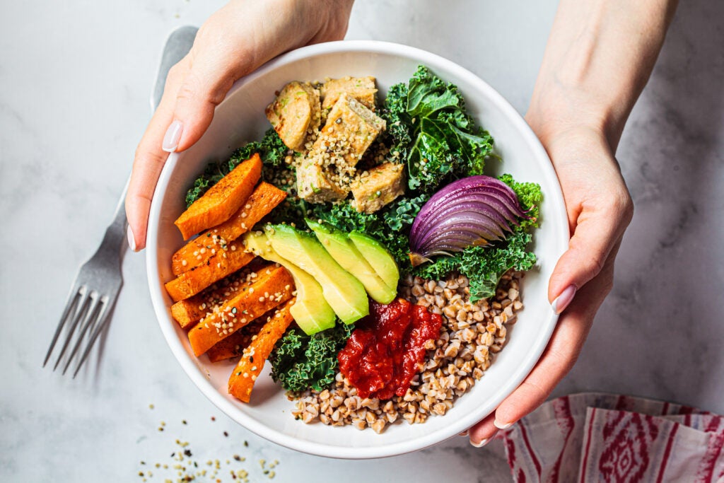 Hands clasping a colorful grain bowl.