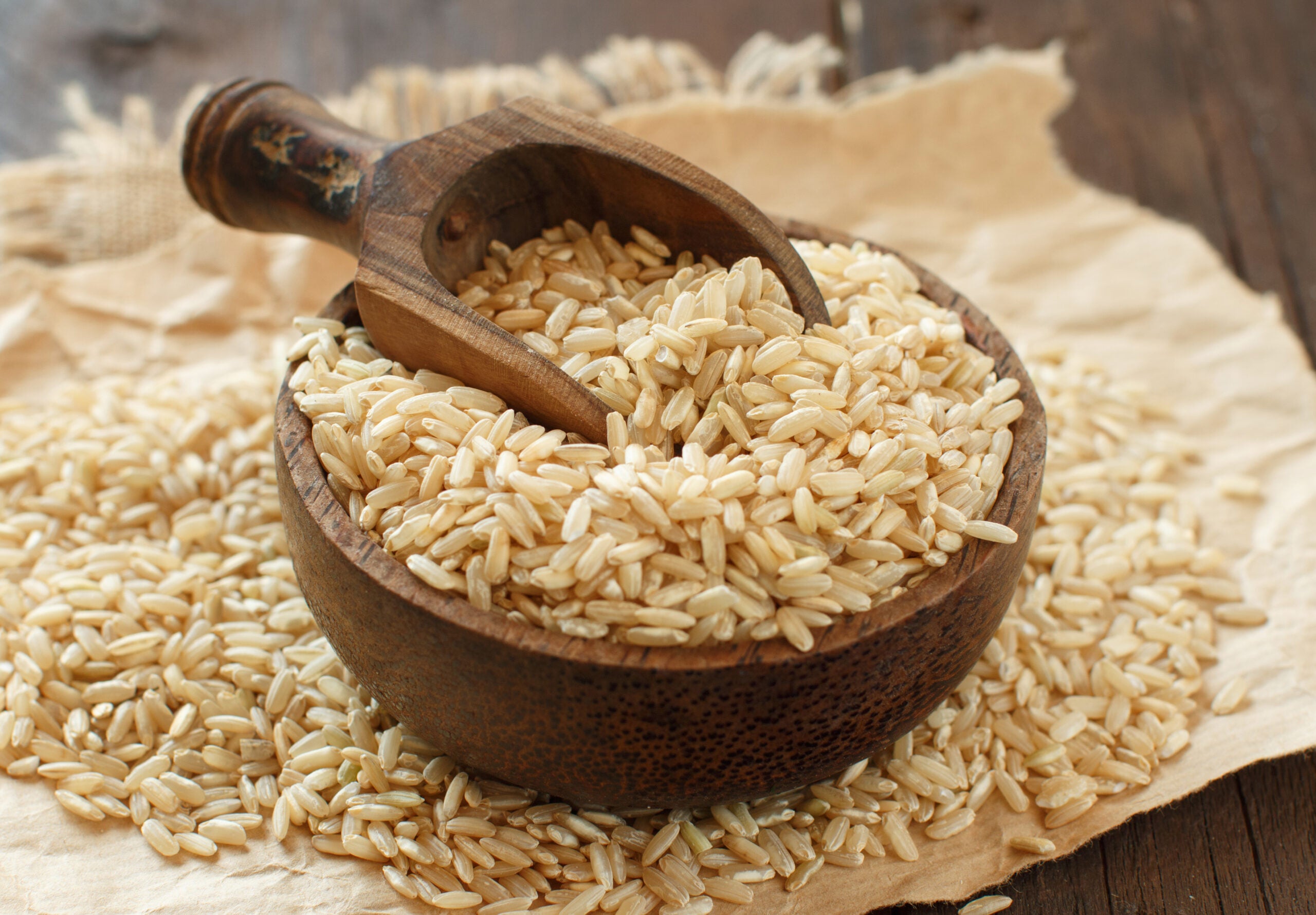 Brown rice, uncooked in a bowl with some outside the bowl.