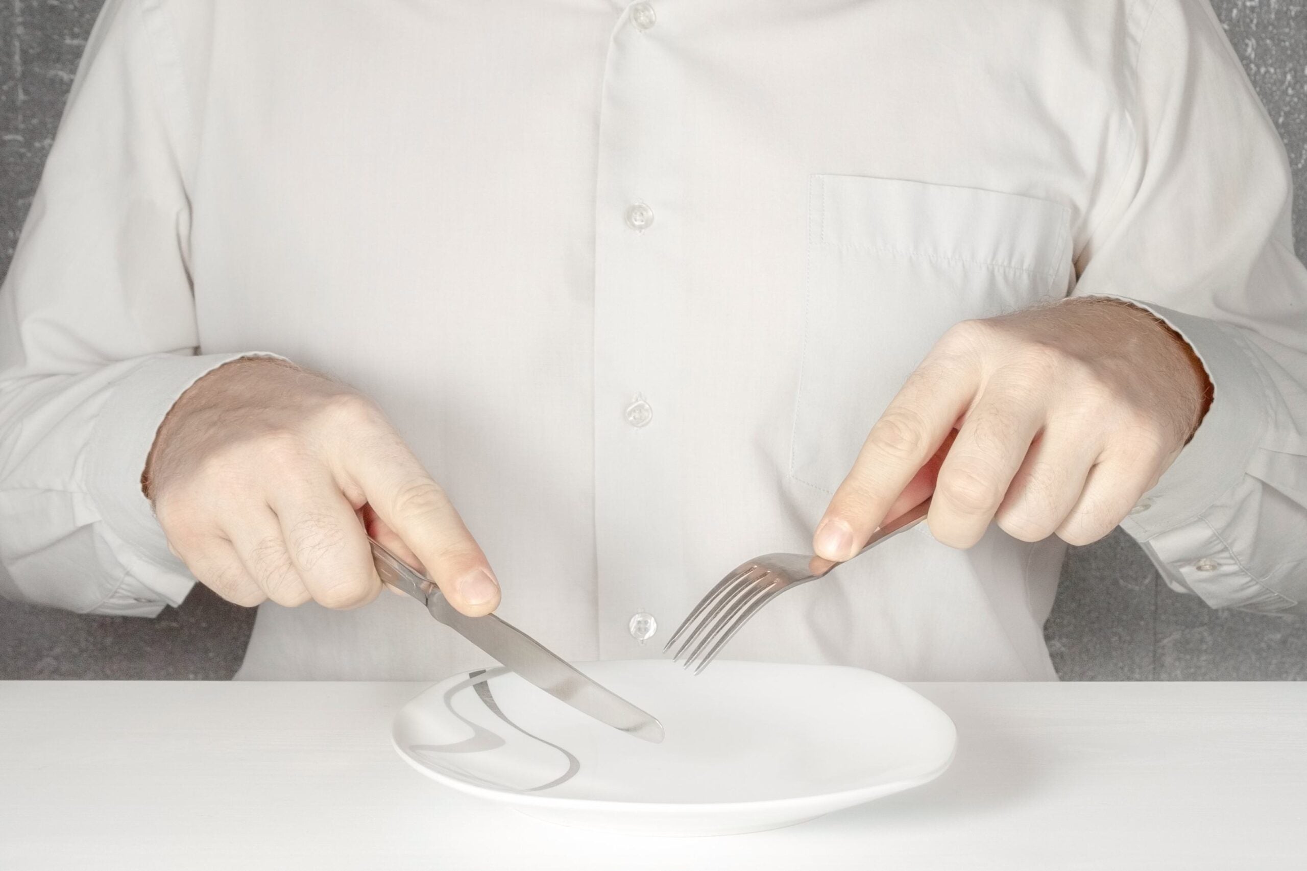 Torso with hands holding cutlery over empty plate for fasting entry
