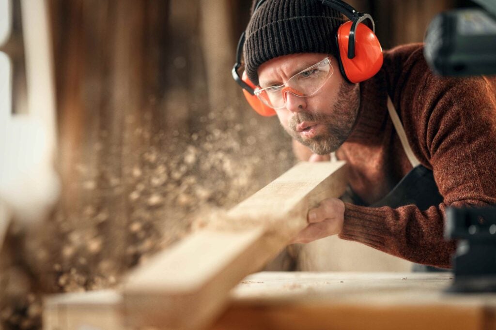 Carpenter blowing wood dust off a plank of wood