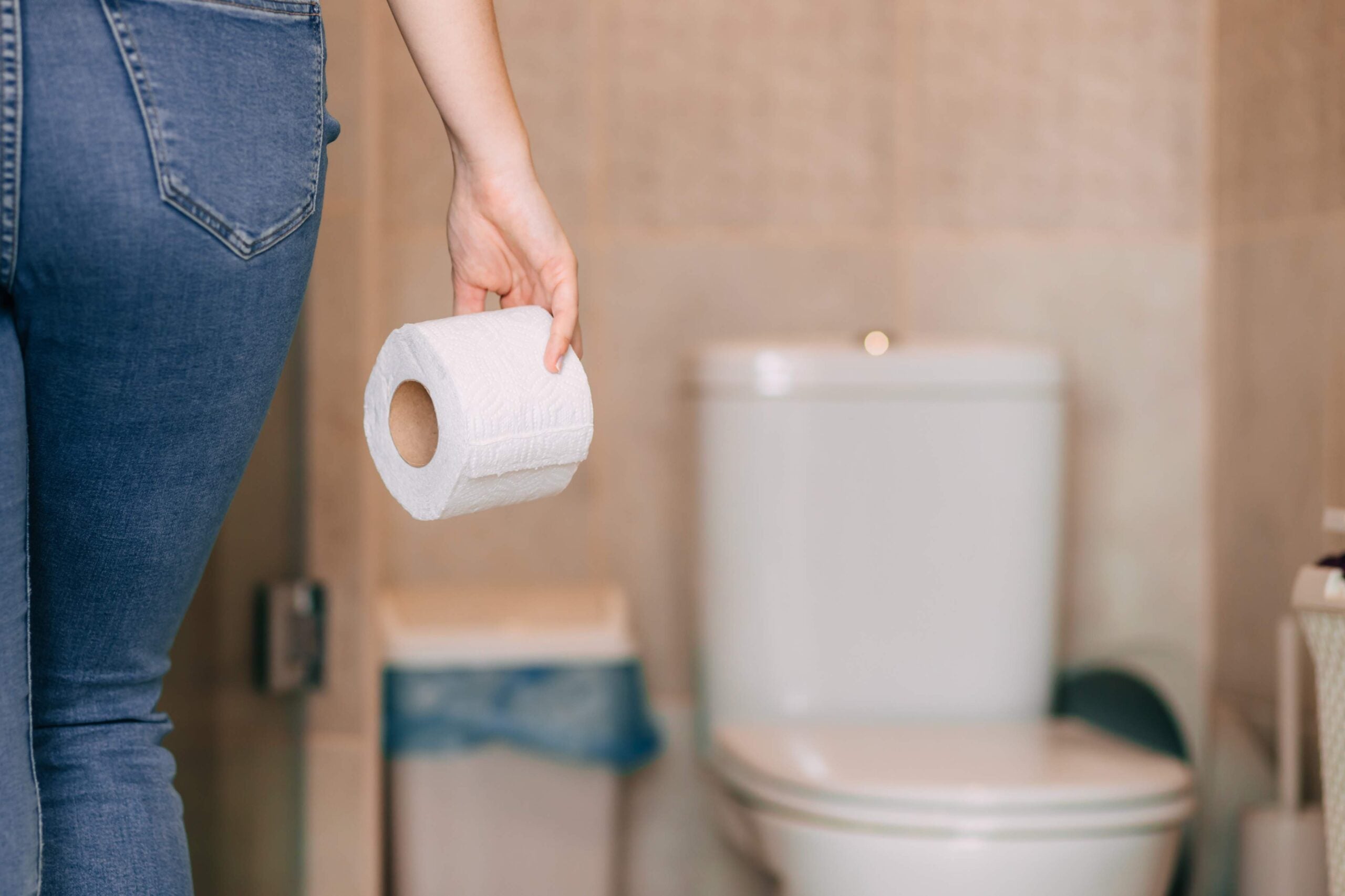 The back of a person holding a roll of toilet paper near a toilet