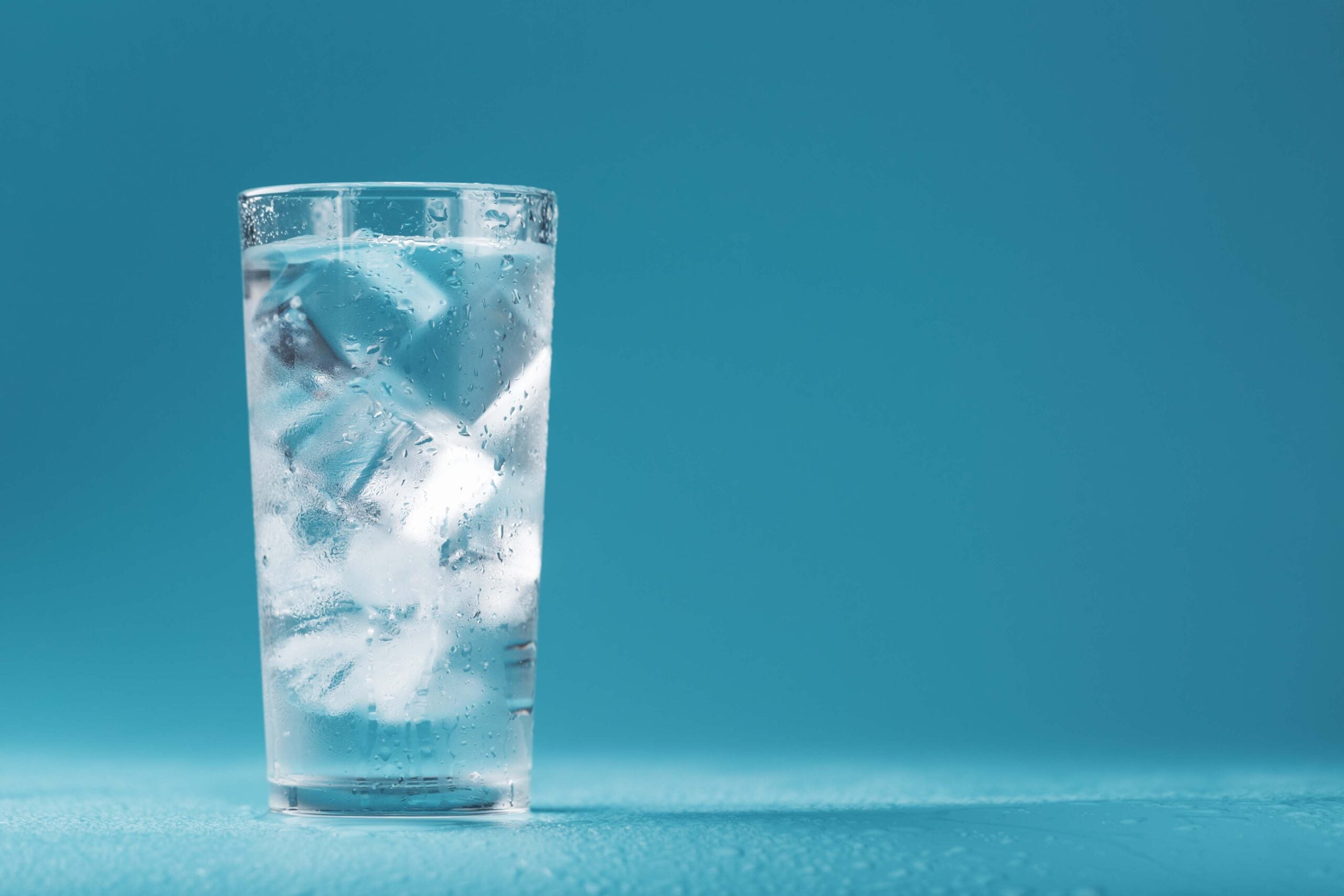 Glass of ice water against a teal background