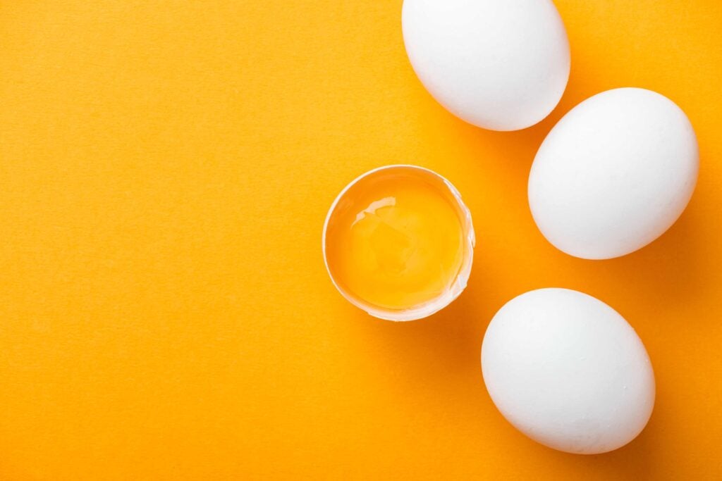 3 and half white eggs on a vibrant yellow/orange background