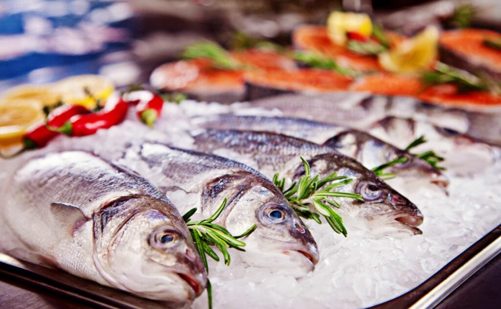 Whole fish on ice with herbs and veggies around them