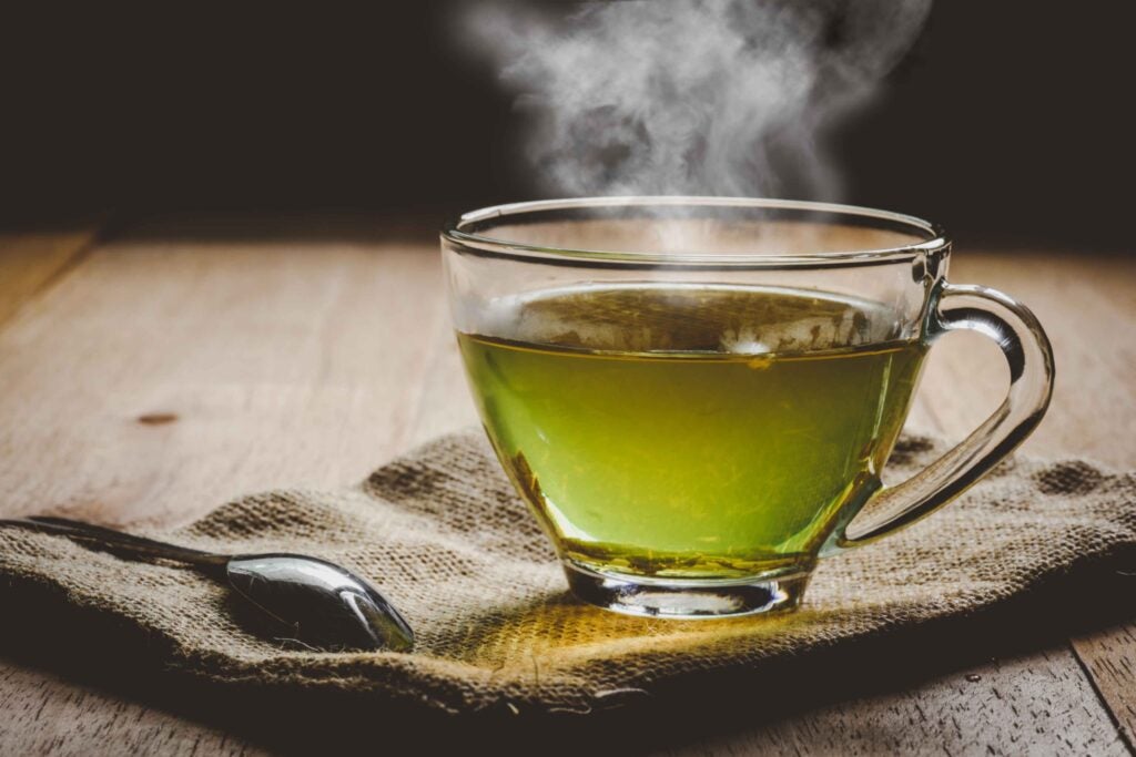A cup of steaming hot green tea in a clear mug