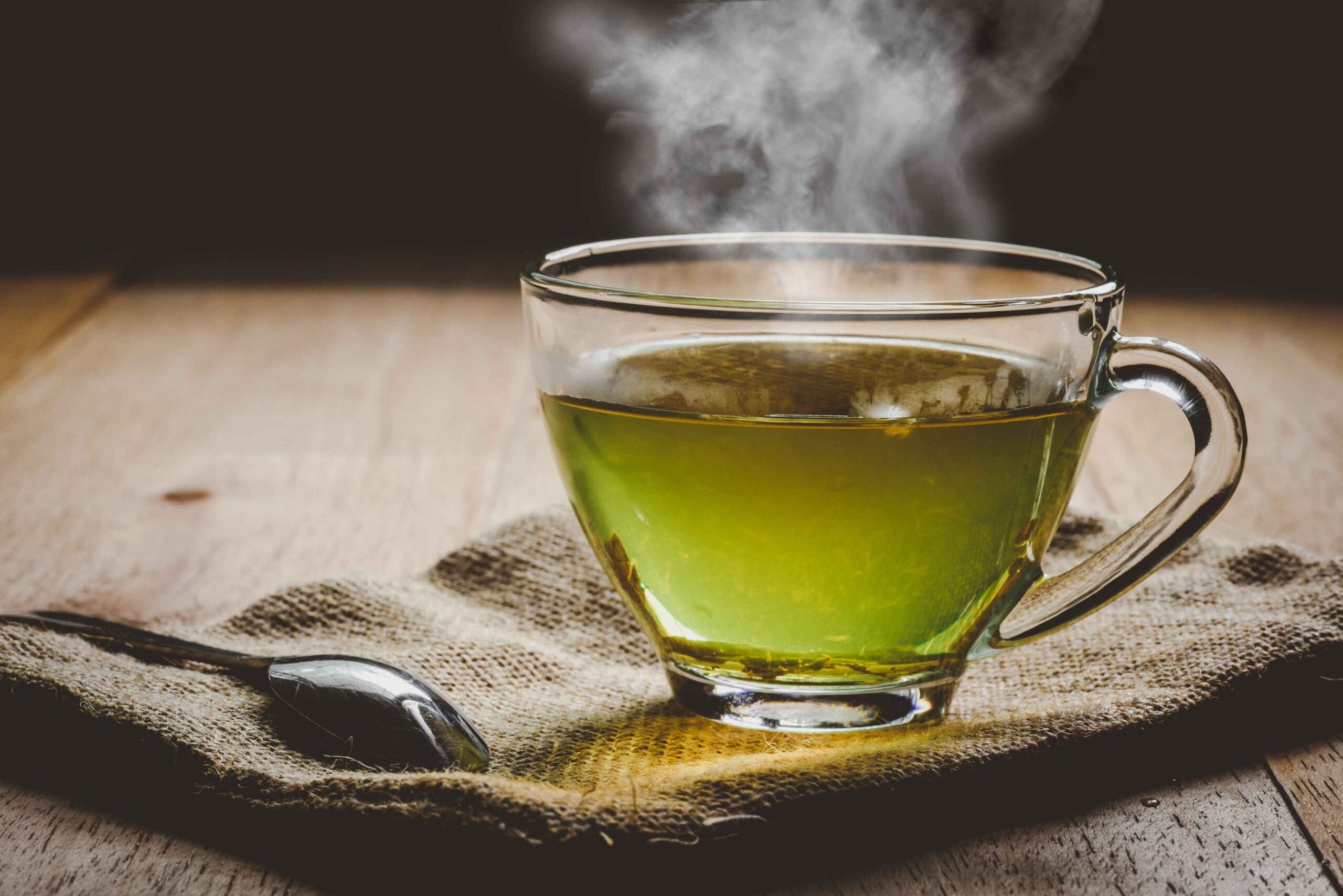 A cup of steaming hot green tea in a clear mug
