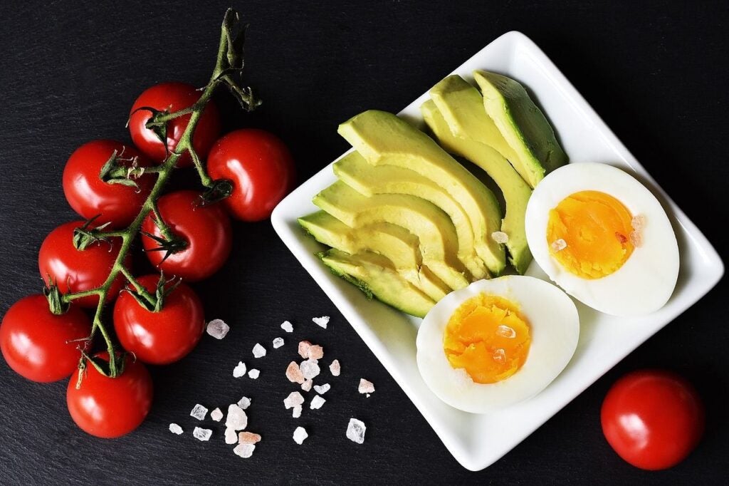 Plate of a hard-boiled egg and avocado with tomatoes on the side