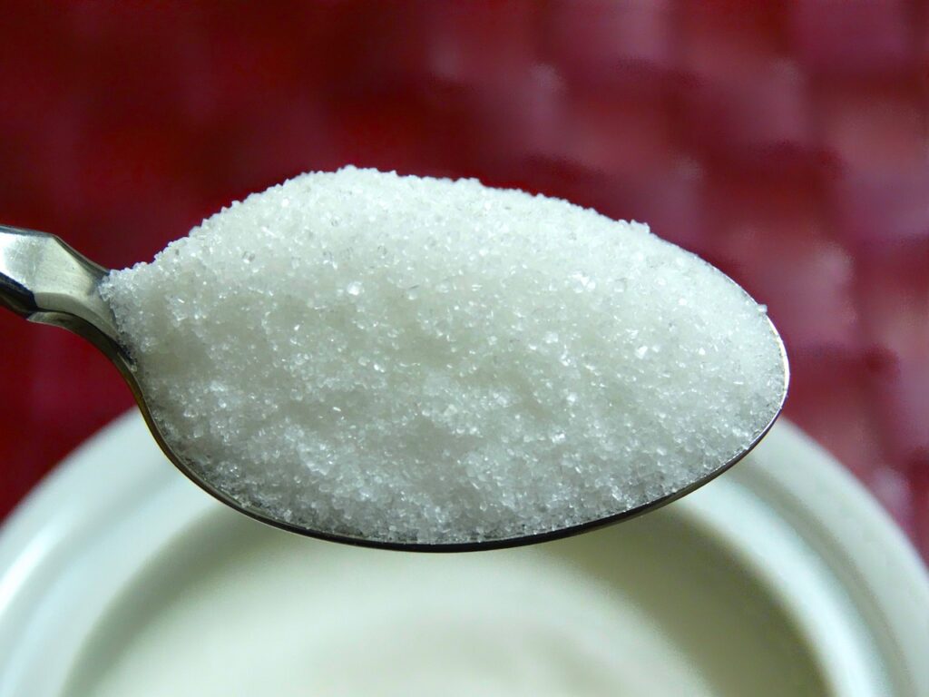 Heaping tea spoon of table sugar hovering over a dish
