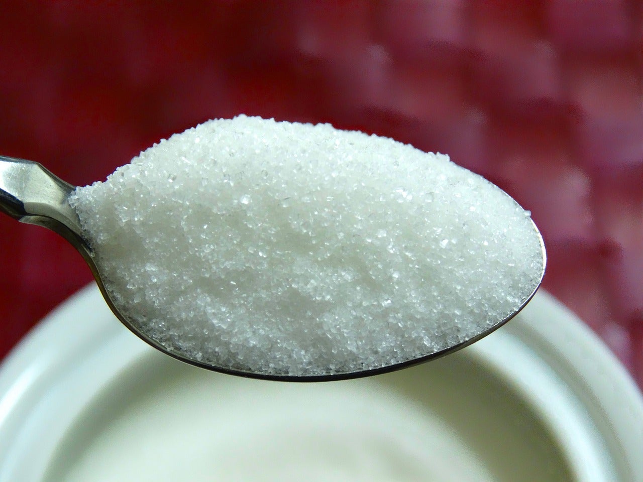 Heaping tea spoon of table sugar hovering over a dish