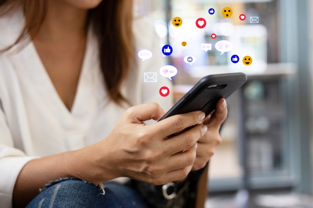 Woman holding phone with social media symbols floating in the air above it.