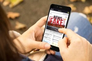 Hands looking at a cell phone that says FAKE over the news the person is reading.