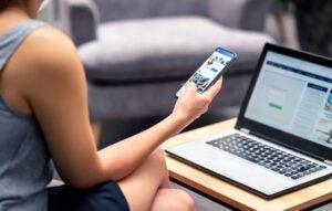 Person holding smart phone seated next to a laptop.