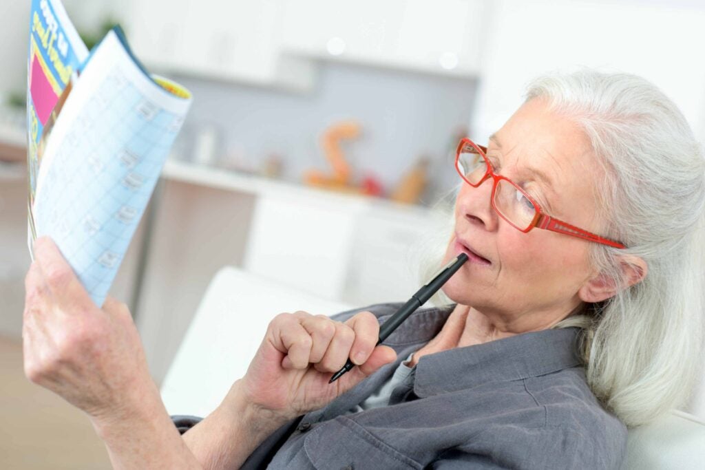 Woman on a couch, holding a writing utensil and a booklet, looking like she's about to take a quiz.
