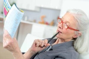 Woman on a couch, holding a writing utensil and a booklet, looking like she's about to take a quiz.